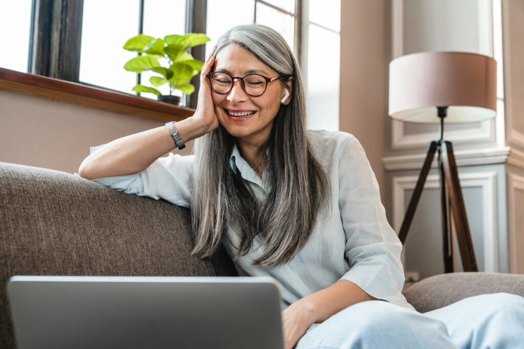 Excited mature woman with grey hair watching movie on laptop at home